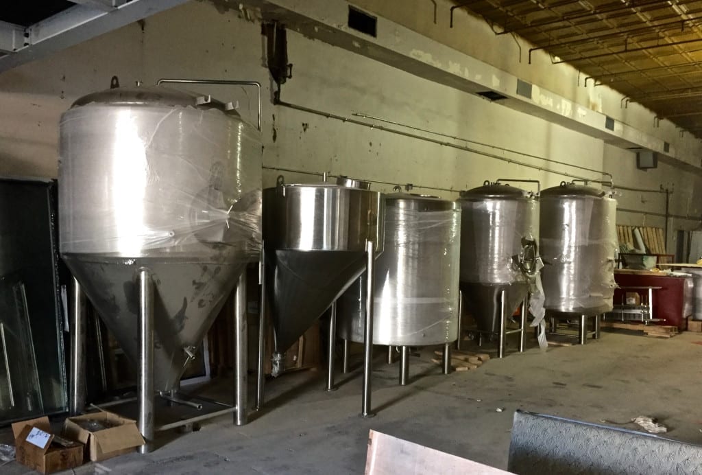 Several fermenters and serving tanks are sitting along the sidewal